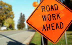 orange diamond-shaped road work ahead construction sign in front of a paved road.