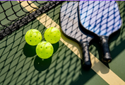 a blue and black pickleball paddle with yellows balls on a green pickeball court